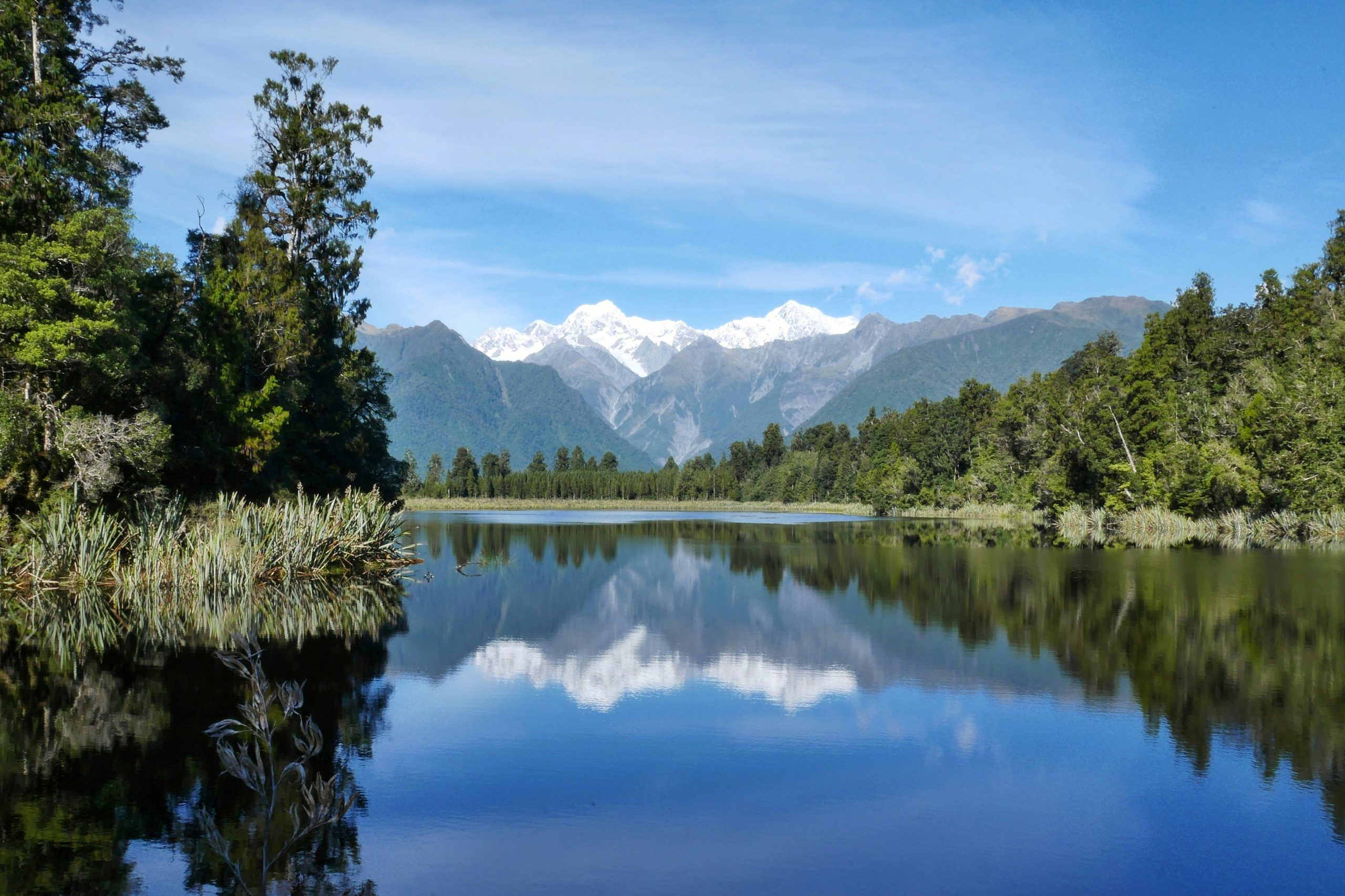 patrick-landscape-unsplash A view of a lake in front of a mountain with trees on the sides.